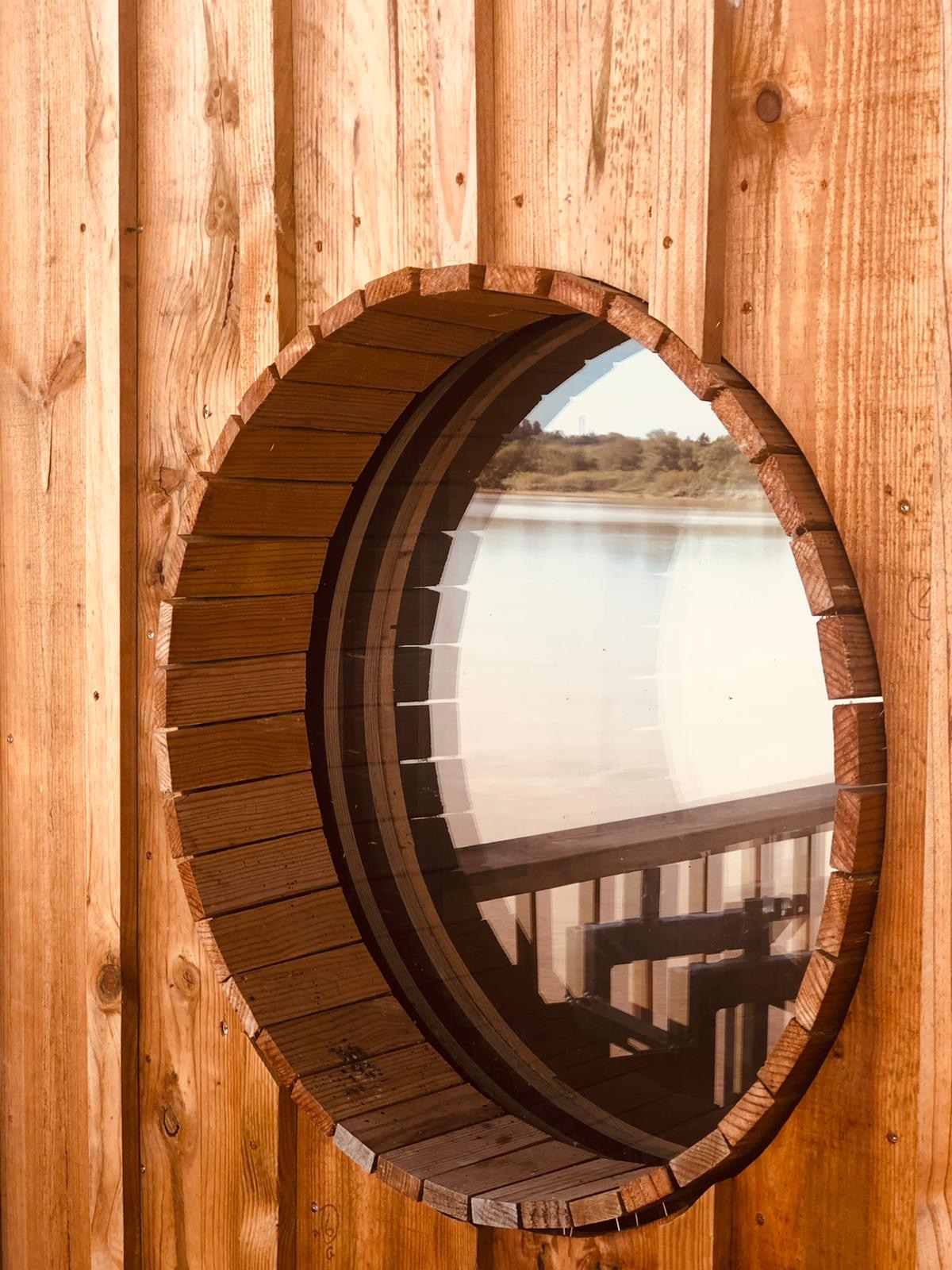 Détail d'un hublot rond en bois sur la façade de la cabane, assemblage à lattes verticales